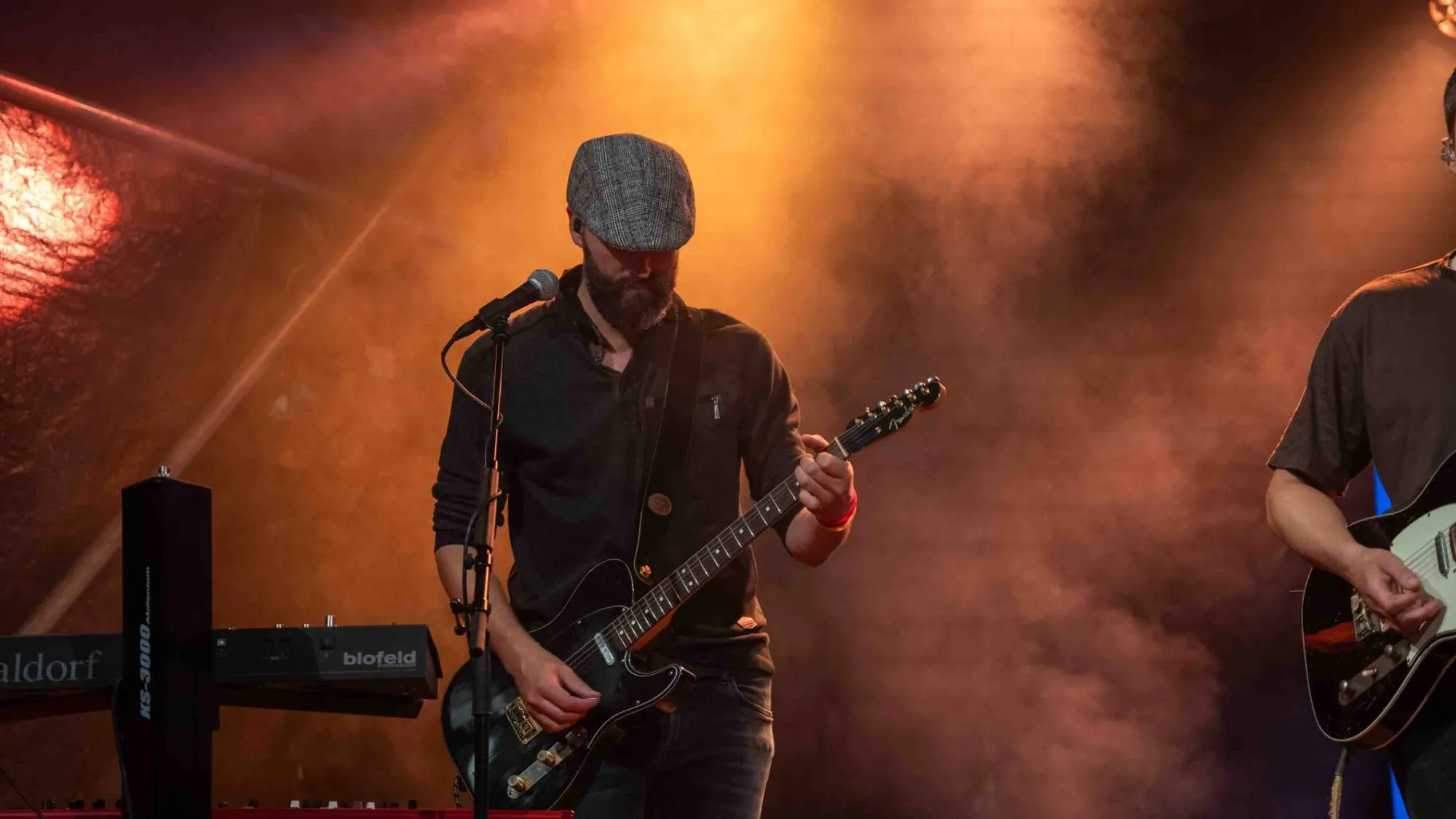 Muziekfotografie van een gitarist met pet in warm podiumlicht